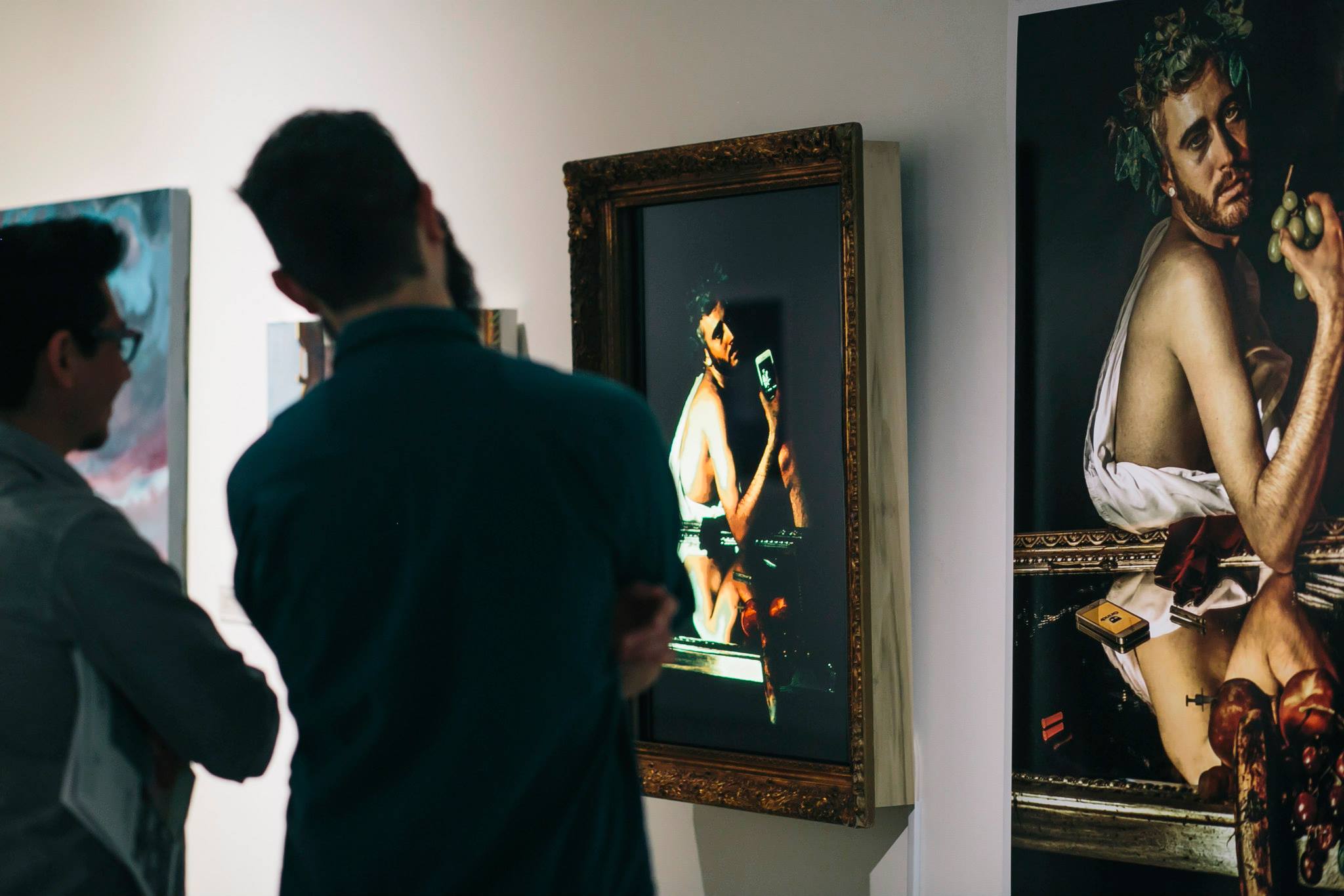 A closer view of the Sick Bacchus framed video monitor beside the large-format print, gallery visitors looking on