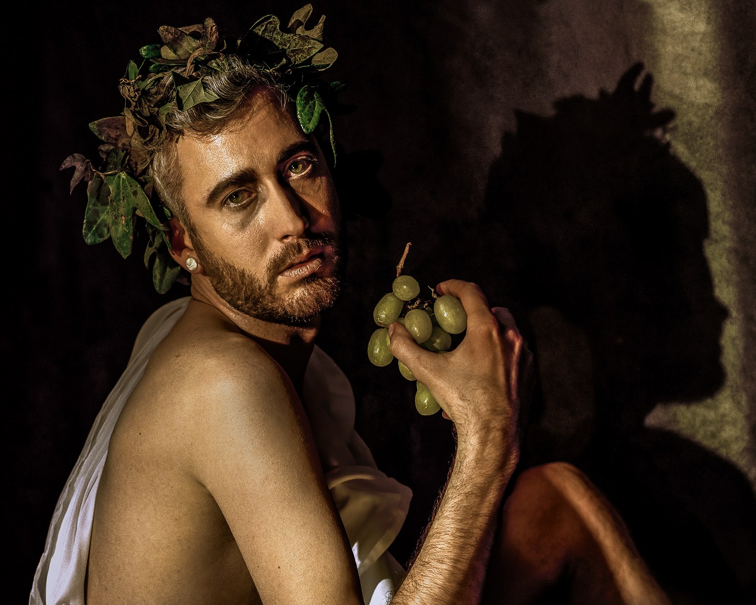 Sick Bacchus, close: the model crowned in vine leaves, holding grapes, in Caravaggio’s pose.